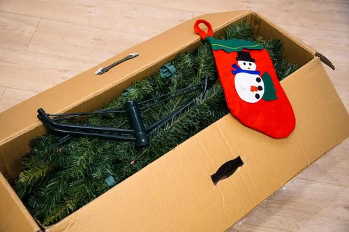 An artificial Christmas tree and snowman stocking folded in a cardboard box.