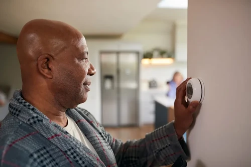 A man adjusts the smart thermostat in his home to save energy during winter.