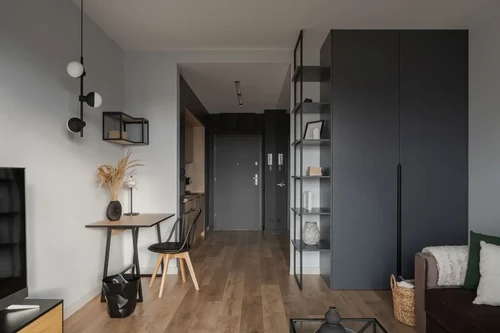 A stylish but small gray and white apartment with a couch, TV, writing desk, and galley kitchen.