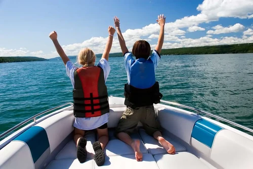 Two kids are at the front of a boat, wearing lifejackets.