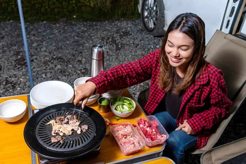 Young woman grilling meat outside of RV.