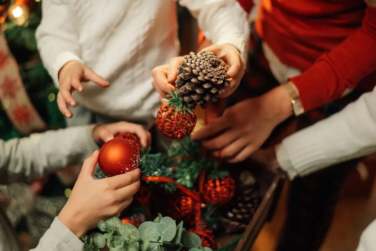 Hands packing red ornaments and pinecones into a box, preparing fragile Christmas decorations for seasonal storage. 