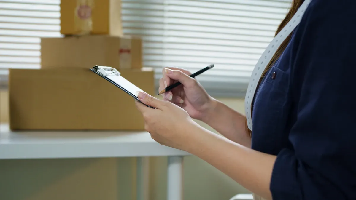 person taking inventory for storage by marking paper on clipboard